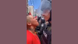 Fact Check: Video Of Smiling Riot Policeman Pepper Spraying Woman With Shaved Head Is NOT Real -- It's From A 'Sora' Account That Features Text-To-Video AI Clips